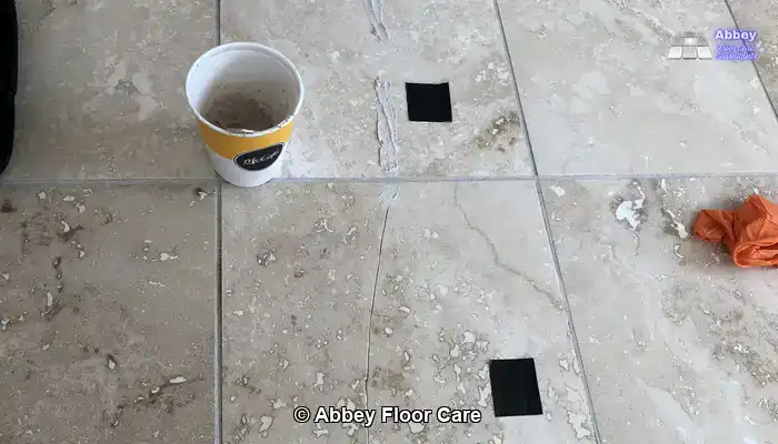 Homeowner repairing cracks in a travertine floor with a small amount of cement grout.
